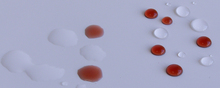 Wasser und Rotwein auf einer partiell mit WAYTONA® Keramikversiegelung versiegelten (rechte Seite) Wandfliese. Deutlich zu erkennen der Abstoßeffekt der nanoversiegelten Oberfläche.